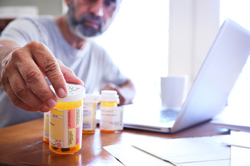 Man sitting at computer looking at prescription medication bottles